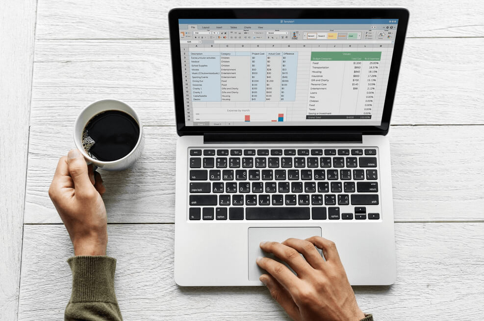 A person holding a coffee cup while working on a laptop with a spreadsheet on the screen, showcasing image.