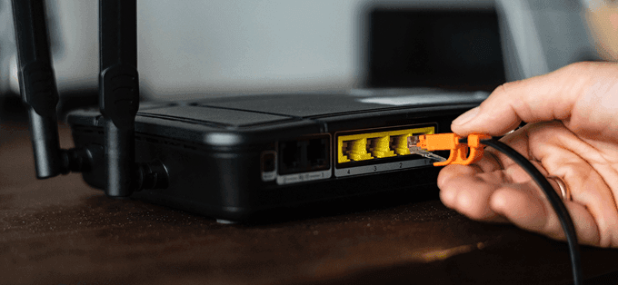 A hand connecting an orange Ethernet cable to a black router, illustrating image.